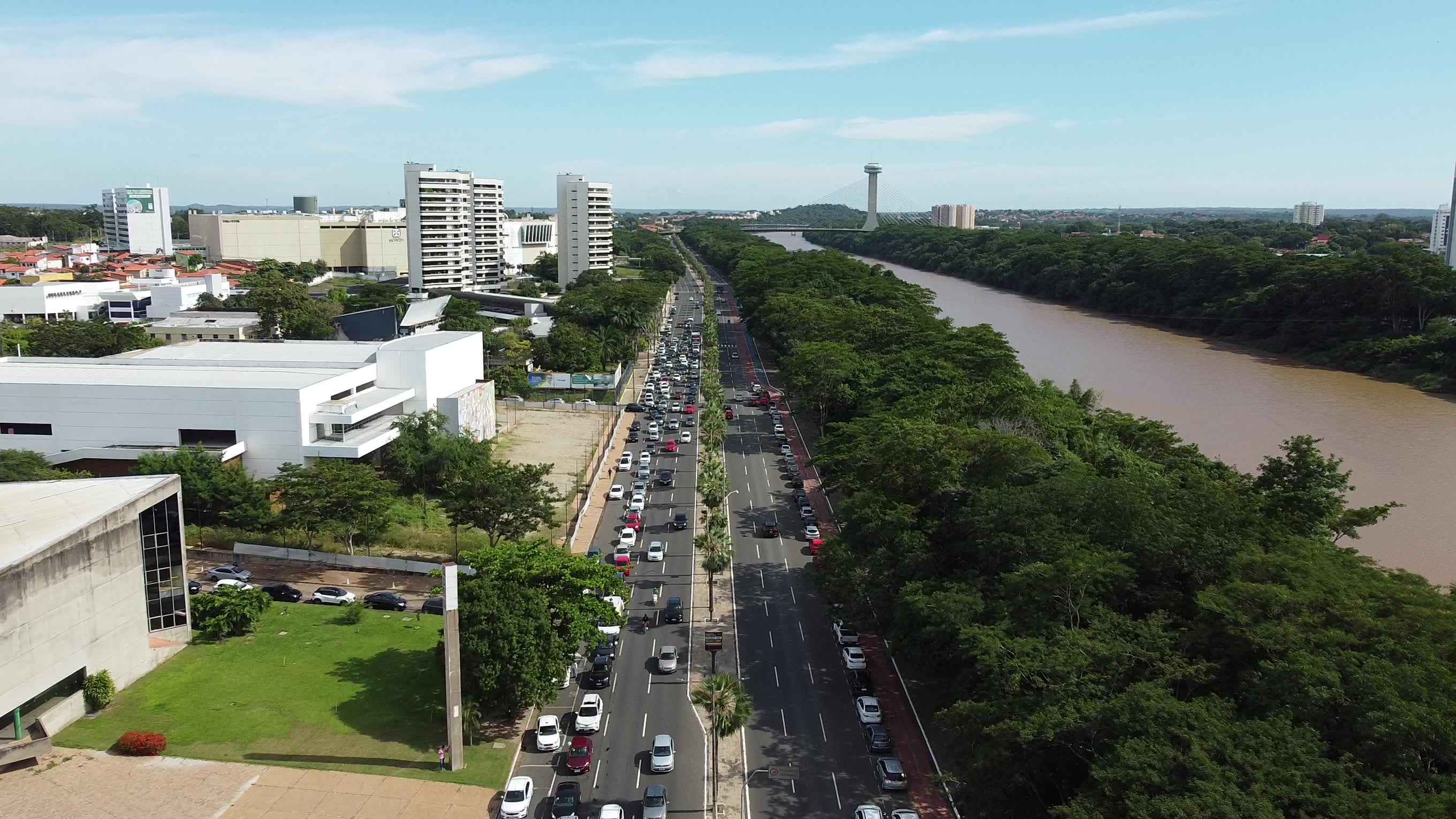 Avenida com grande movimentação mostrando rio e ponte estaiada.